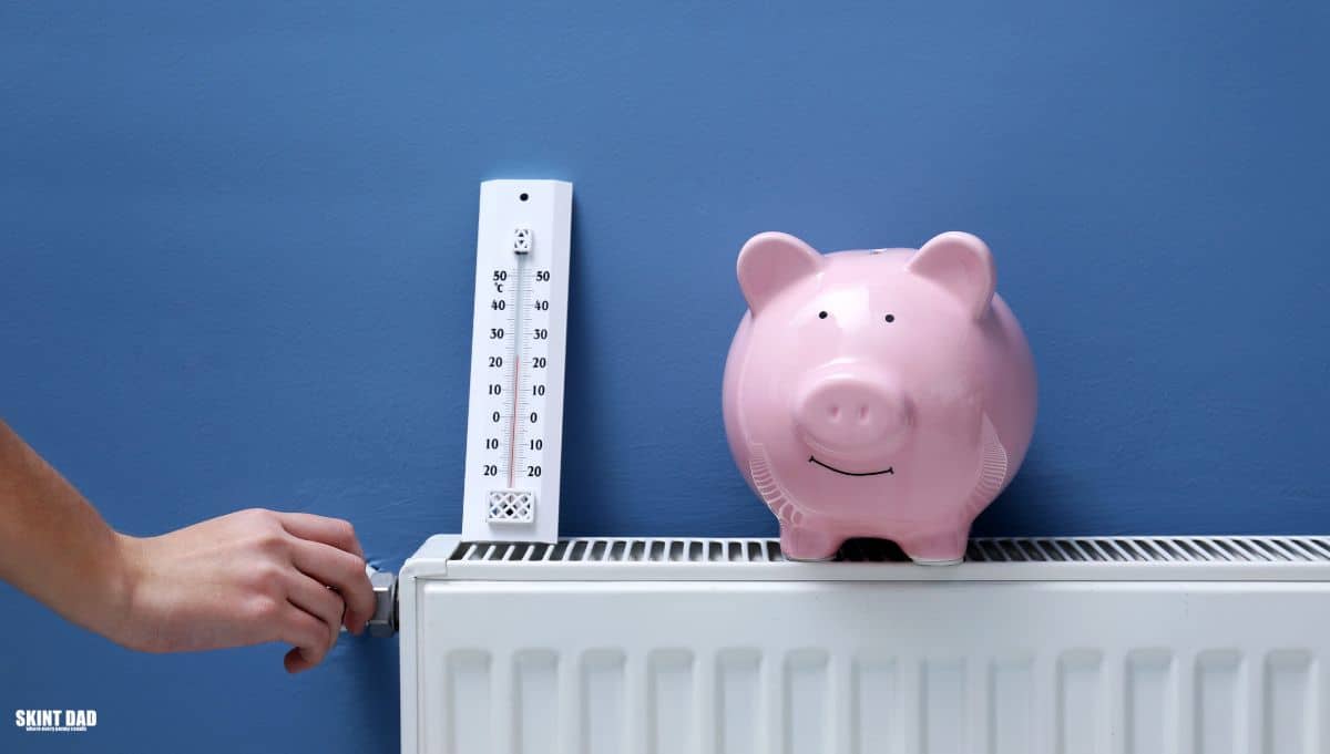 A hand adjusts a radiator valve beside a thermometer and pink piggy bank