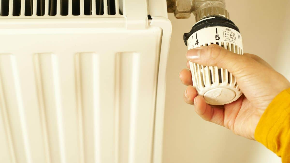 A hand adjusting the temperature control on a radiator.