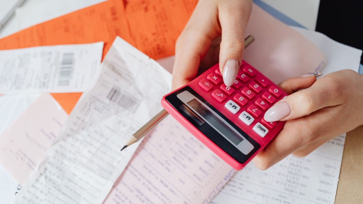 Person using a pink calculator while checking receipts and household paperwork