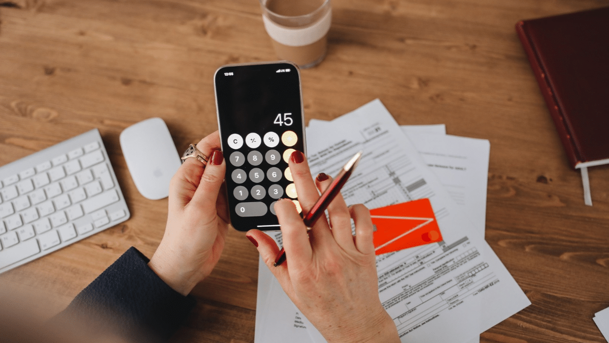 Person using a phone calculator while reviewing financial paperwork