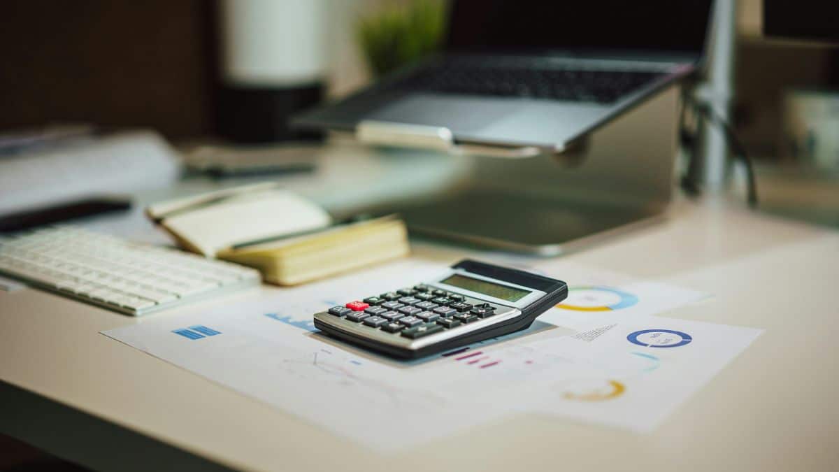 Calculator on financial paperwork beside a laptop