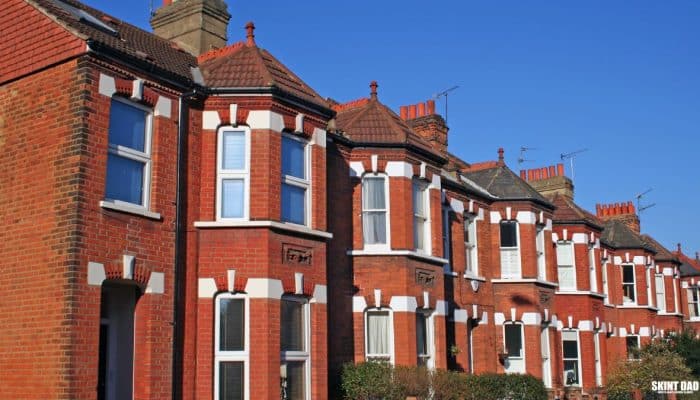 Row of red-brick terraced houses with bay windows under a blue sky.