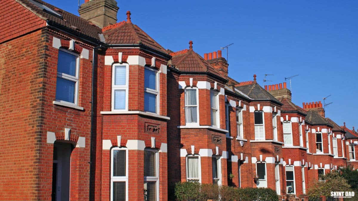 Row of red-brick terraced houses with bay windows under a blue sky.