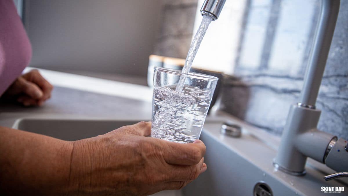 Person filling a glass with water from a kitchen tap